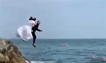 عروسان يحتفلان بزواجهما بالقفز فى البحر مرتدين ملابس الزفاف.. فيديو 